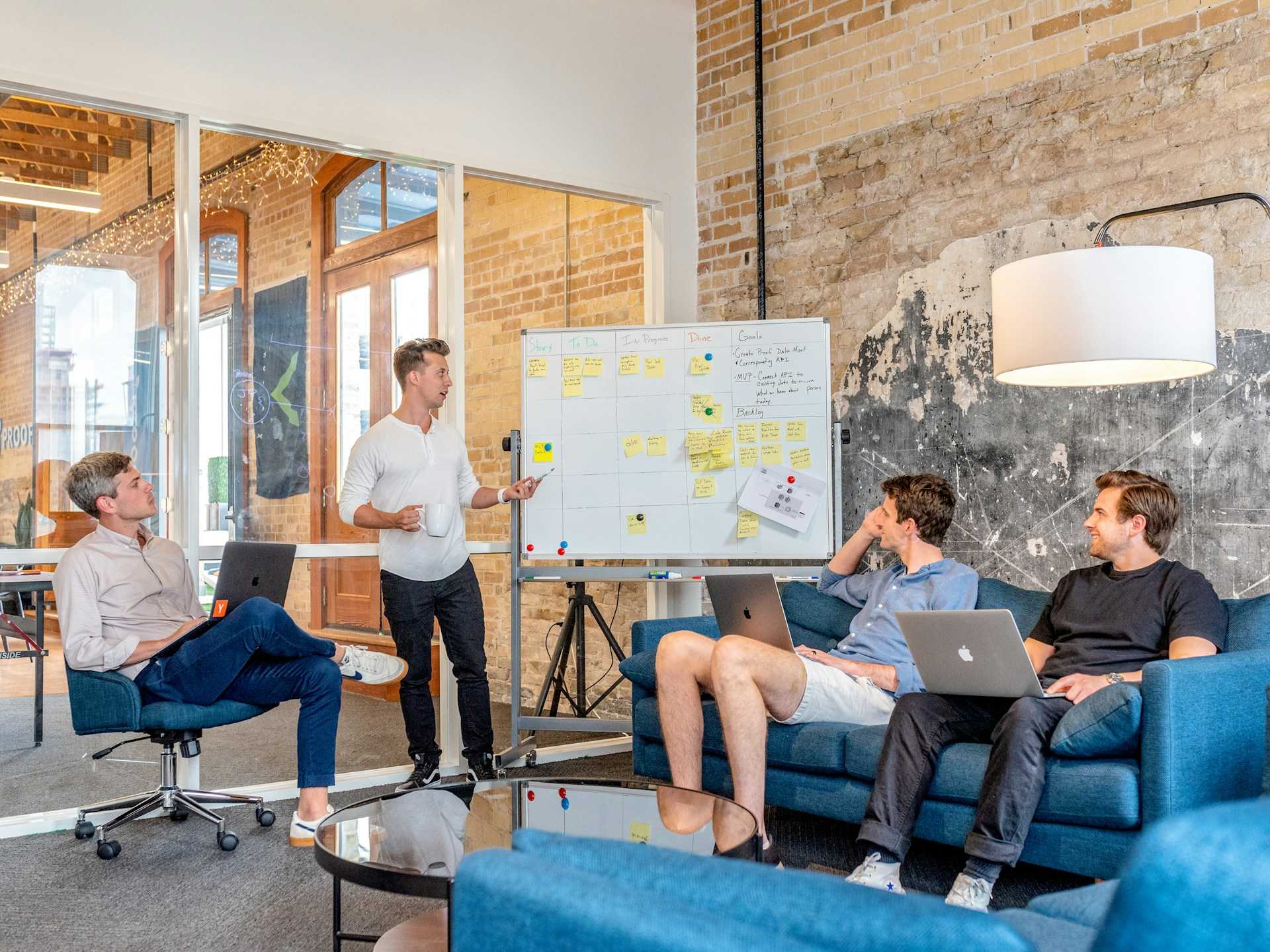 Three men sitting while using laptops and discussing something beside a whiteboard